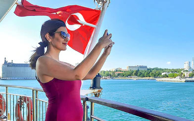 Woman taking photo on ferry with Turkish flag, Istanbul Asian Side in background.