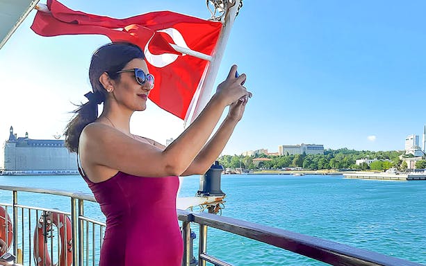 Woman taking photo on ferry with Turkish flag, Istanbul Asian Side in background.
