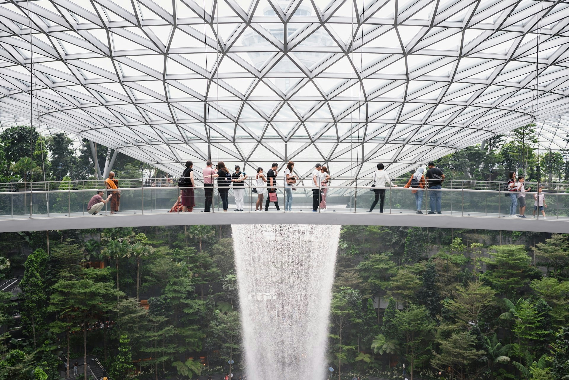 Visitors on the Canopy Bridge at Jewel Changi Airport with waterfall and lush greenery below.