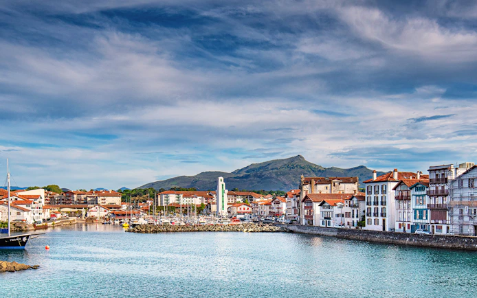 Harbor view of Saint Jean de Luz with traditional Basque architecture and distant mountains.