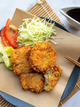 Fried Japanese croquettes with cabbage and tomato slices on a plate.
