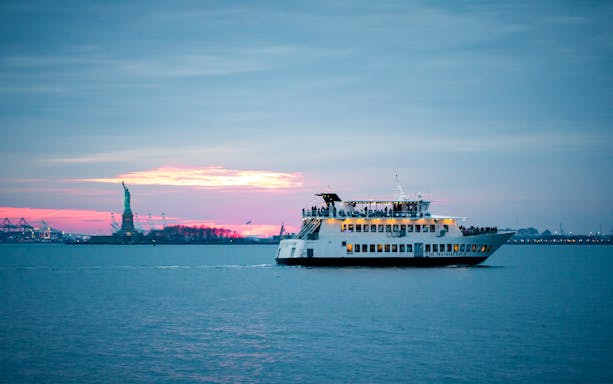 Cruise ship near Statue of Liberty at sunset, New York City.