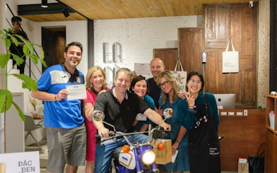 Group enjoying Vietnamese coffee workshop, posing with certificates and a vintage motorcycle.