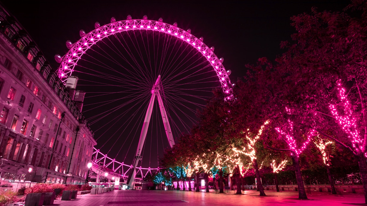 London Eye illuminated at night with vibrant pink lights, view from the riverside walkway.