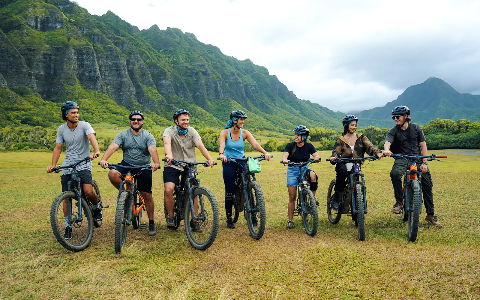 Group of cyclists on e-bikes at Kualoa Ranch with lush mountains in the background.