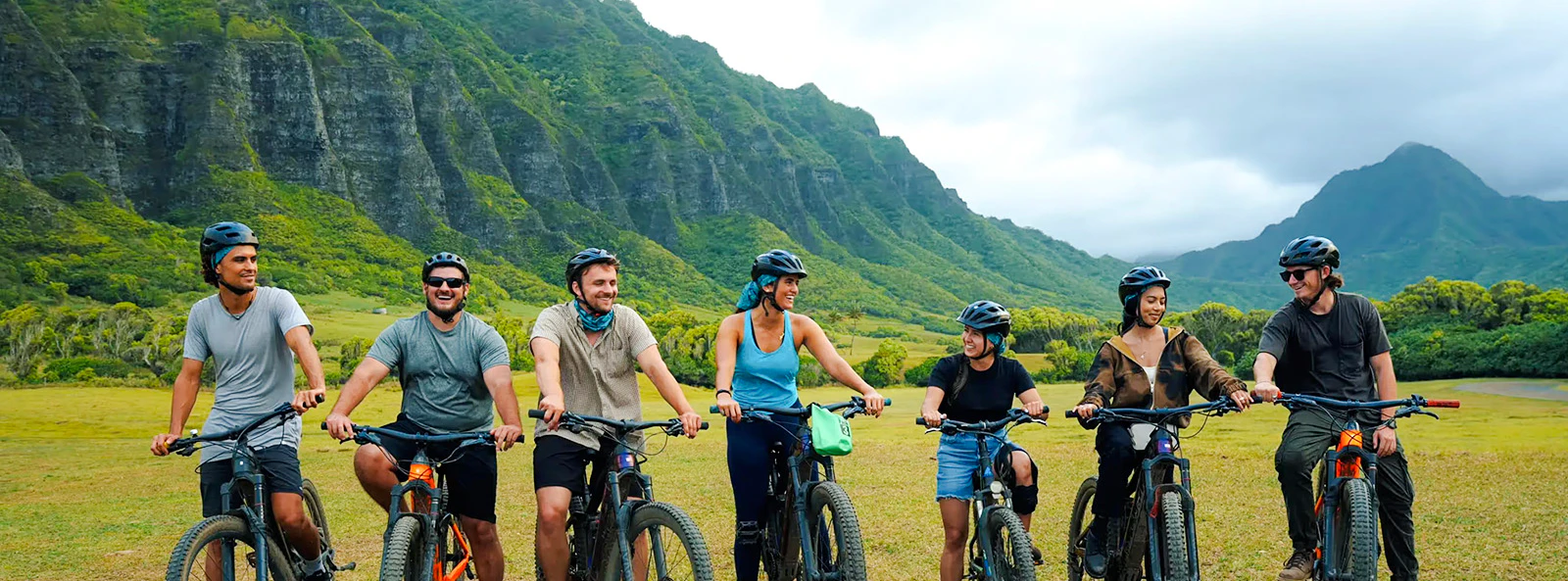 Group of cyclists on e-bikes at Kualoa Ranch with lush mountains in the background.