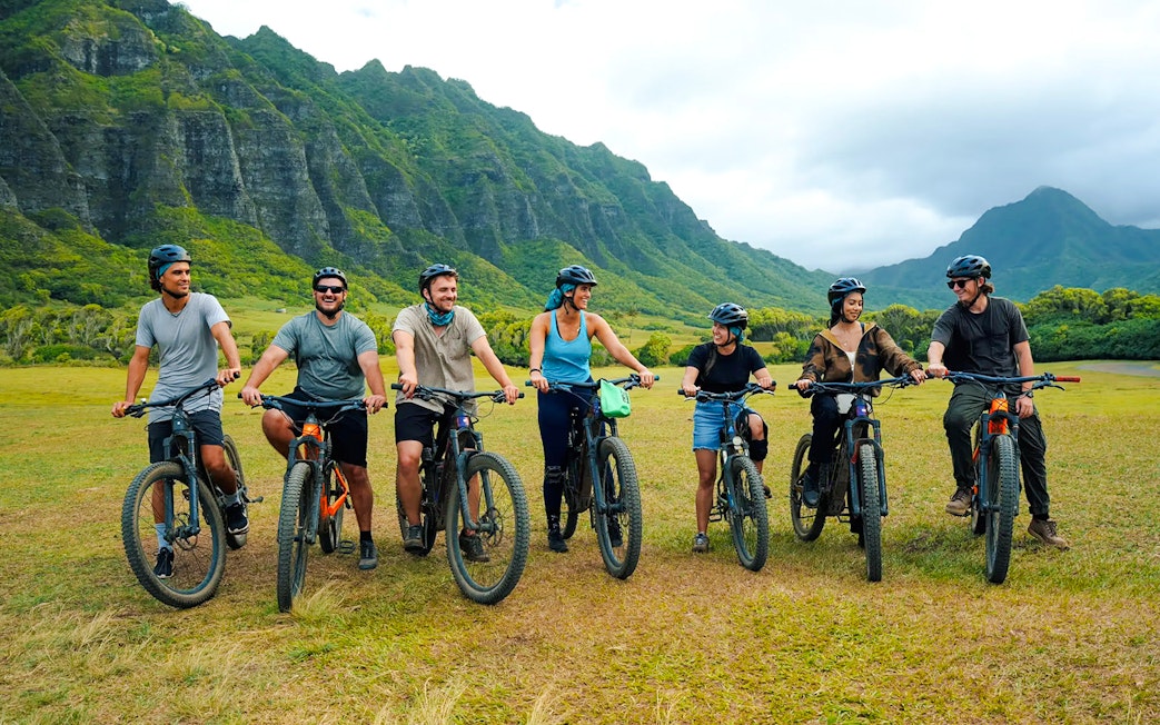 Group of cyclists on e-bikes at Kualoa Ranch with lush mountains in the background.