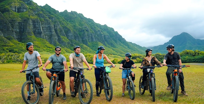Group of cyclists on e-bikes at Kualoa Ranch with lush mountains in the background.