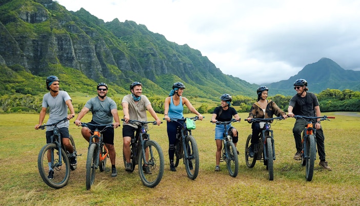 Group of cyclists on e-bikes at Kualoa Ranch with lush mountains in the background.