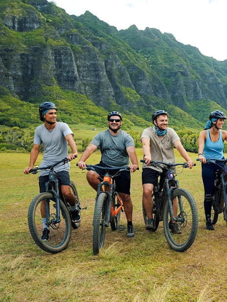 Group of cyclists on e-bikes at Kualoa Ranch with lush mountains in the background.