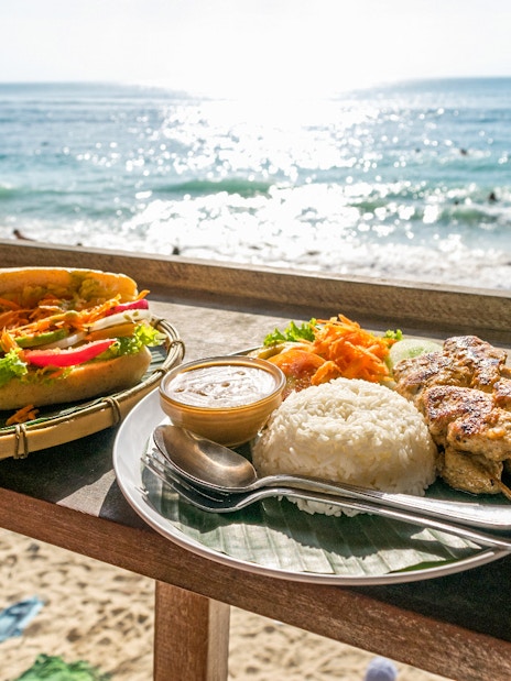 Balinese meal with rice, satay, and drinks on a beachside table in Nusa Penida, Bali.