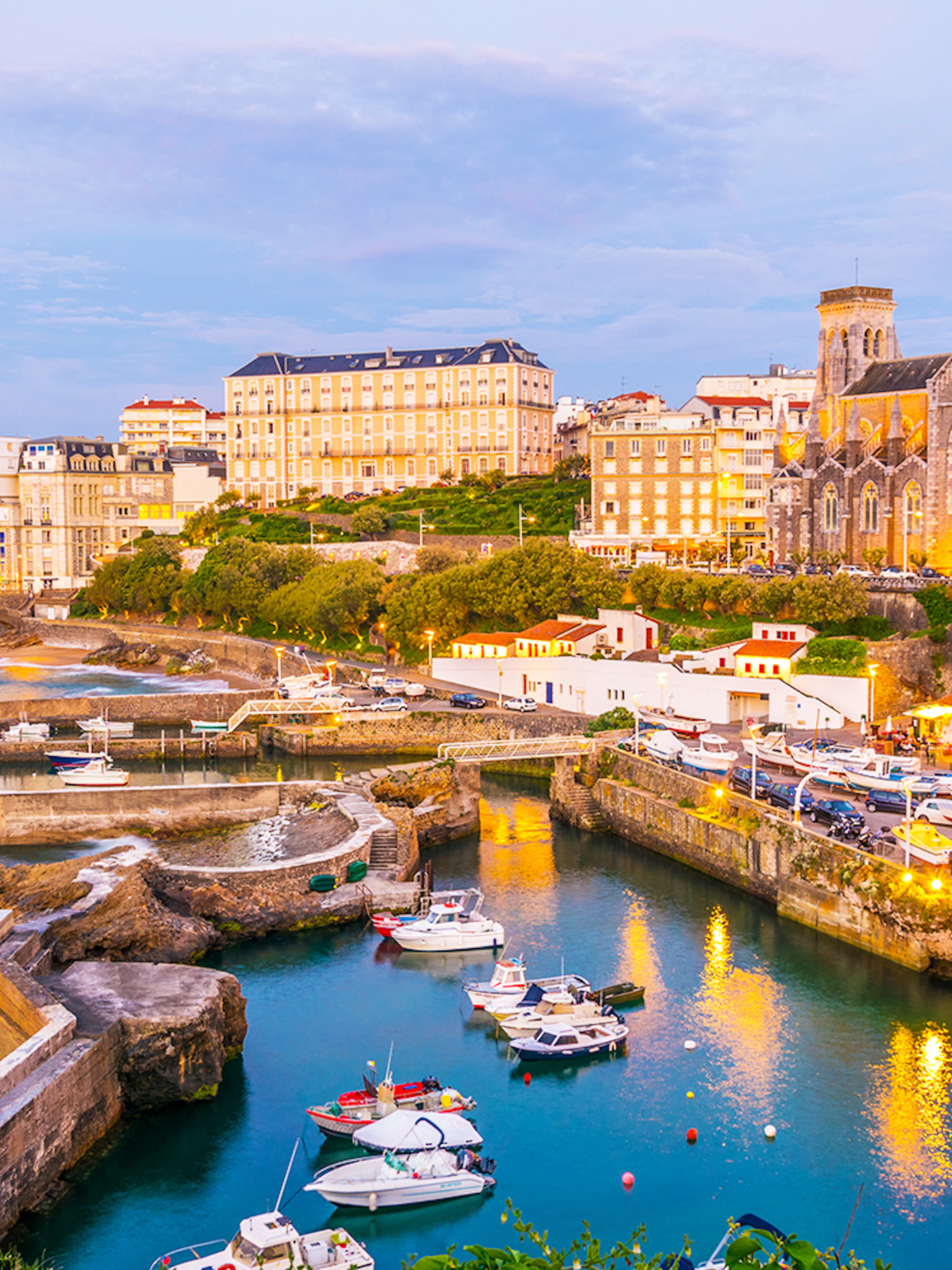 Biarritz harbor with boats and historic buildings at sunset.