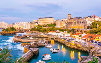 Biarritz harbor with boats and historic buildings at sunset.