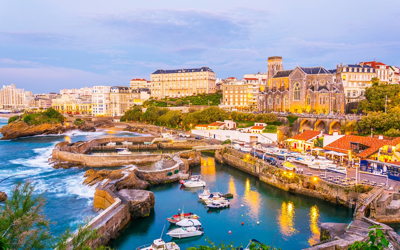 Biarritz harbor with boats and historic buildings at sunset.