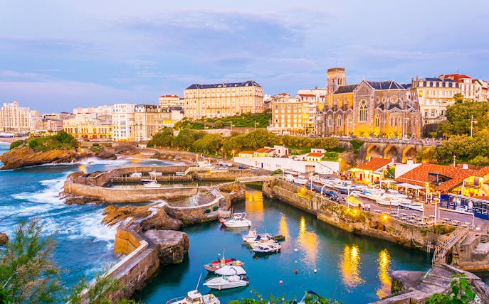 Biarritz harbor with boats and historic buildings at sunset.