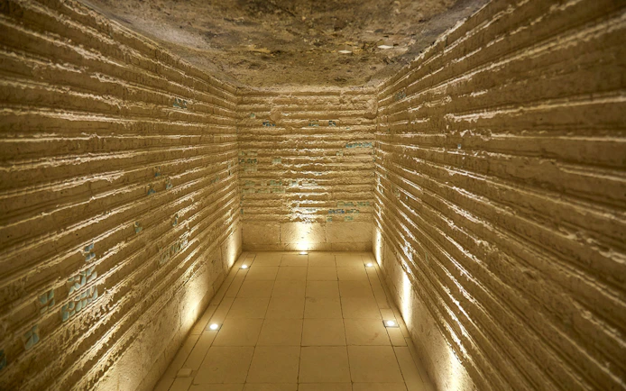 Corridor inside the Step Pyramid of Djoser, Saqqara, Egypt, with illuminated stone walls.
