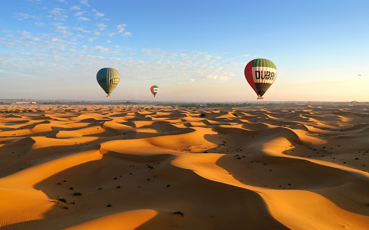Hot air balloons over Dubai desert dunes at sunrise.