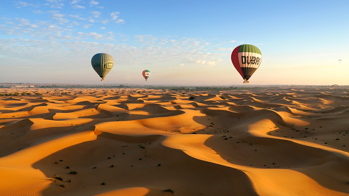 Hot air balloons over Dubai desert dunes at sunrise.