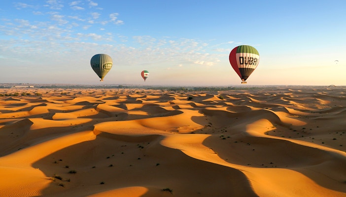 Hot air balloons over Dubai desert dunes at sunrise.