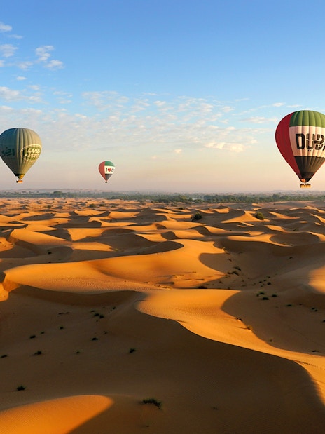 Hot air balloons over Dubai desert dunes at sunrise.