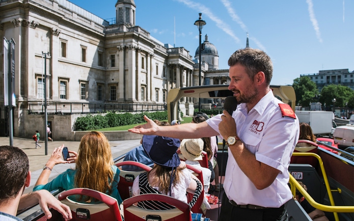 Tour guide speaking to tourists on an open-top bus near the National Gallery, London.