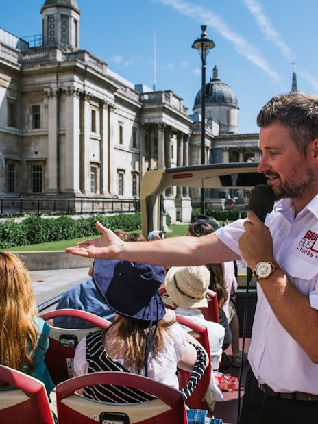 Tour guide speaking to tourists on an open-top bus near the National Gallery, London.