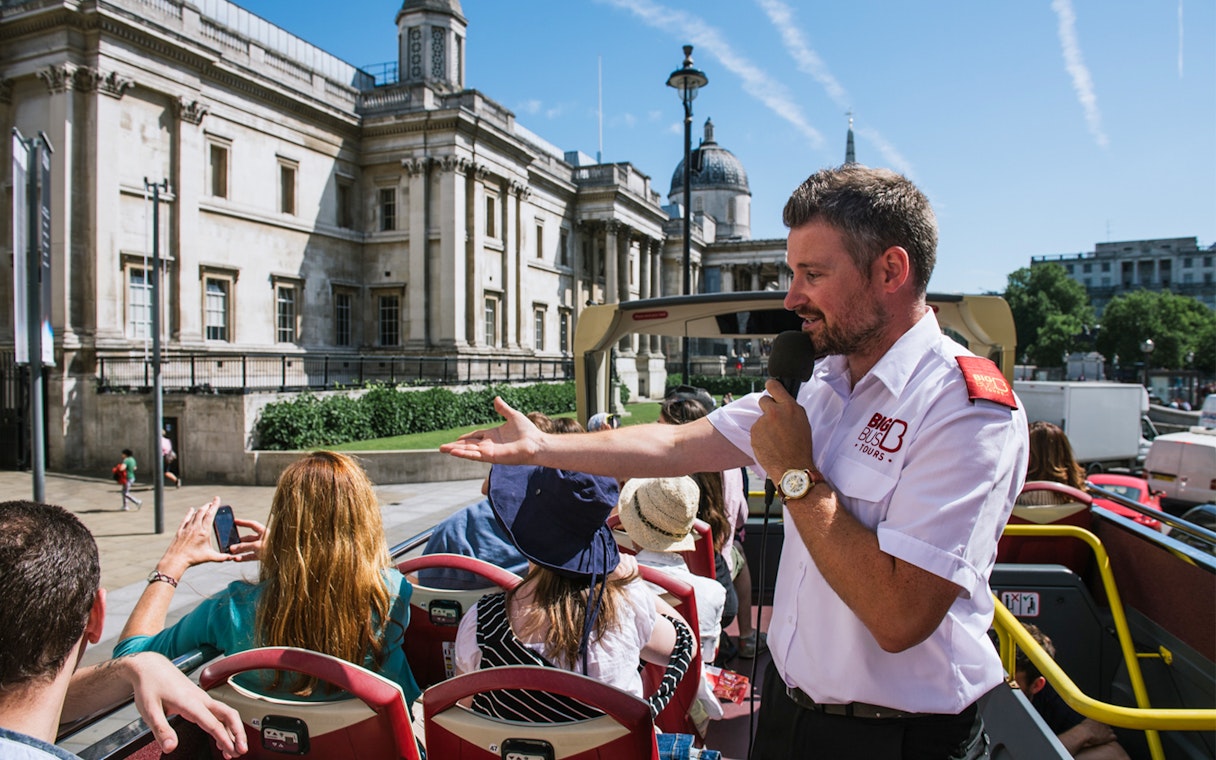Tour guide speaking to tourists on an open-top bus near the National Gallery, London.
