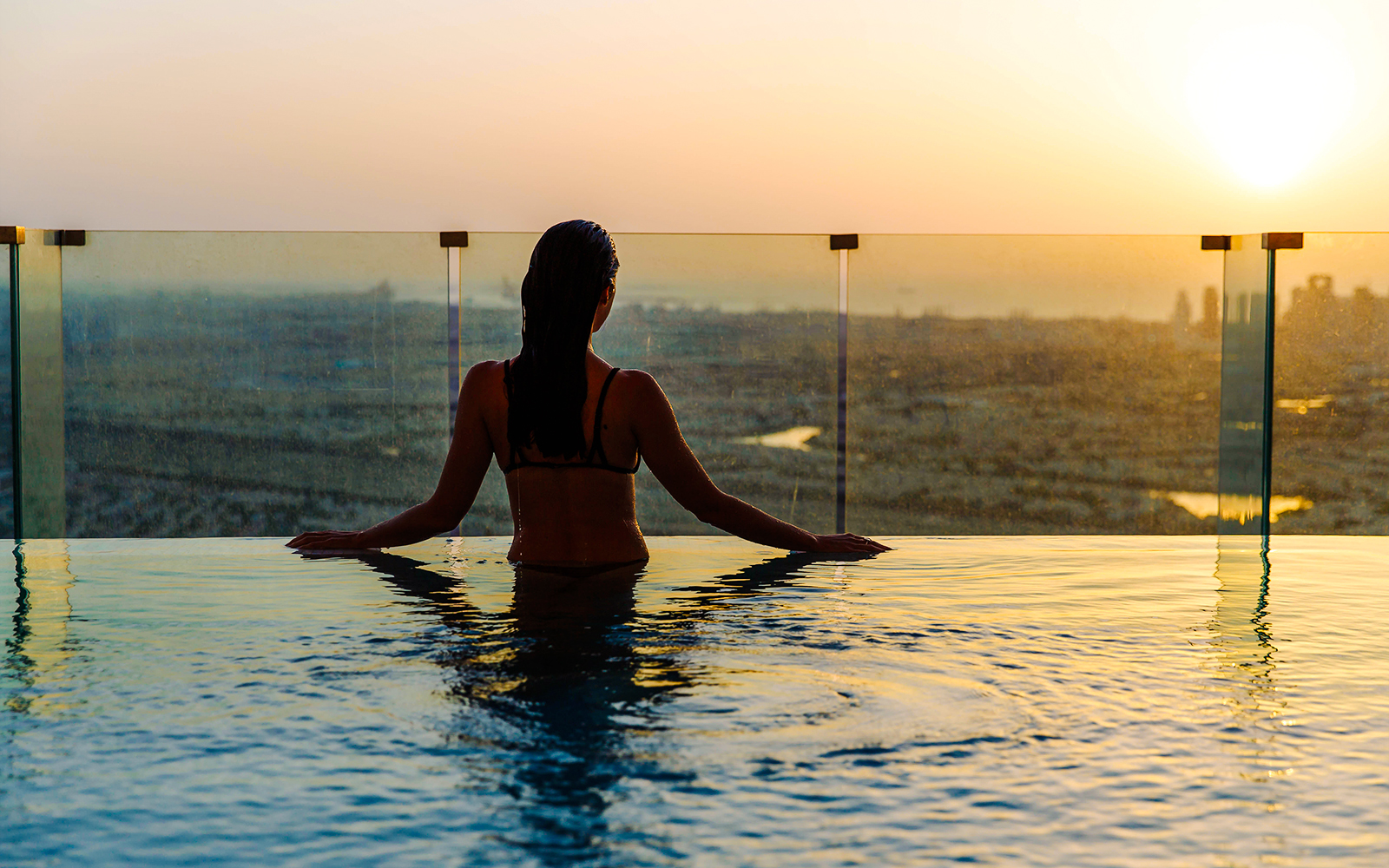 Person relaxing in an infinity pool overlooking Dubai skyline at sunset.