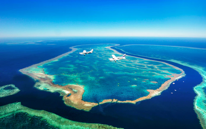 Aerial view of Whitsundays coral reefs with two planes flying over turquoise waters.