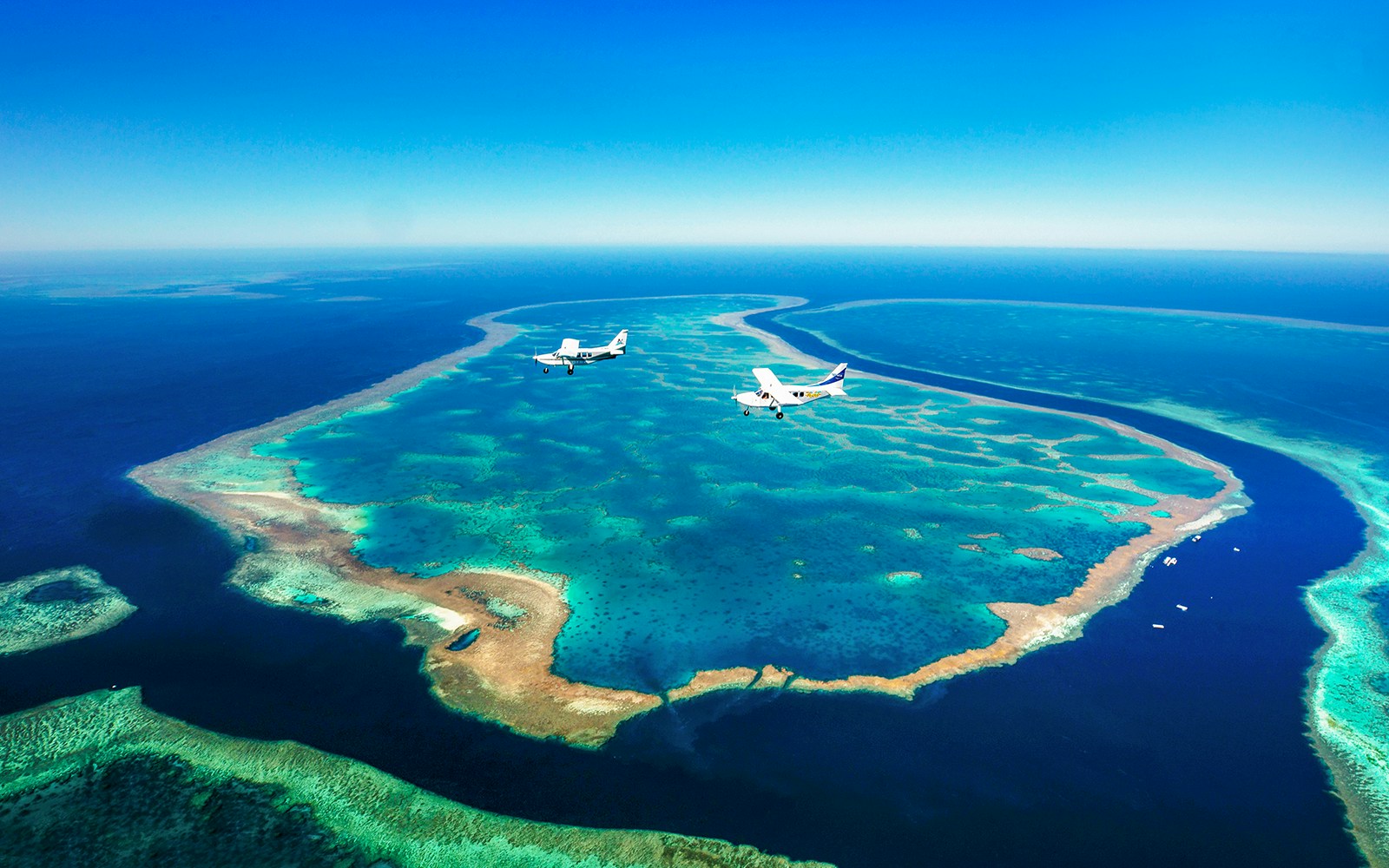 Aerial view of Whitsundays coral reefs with two planes flying over turquoise waters.