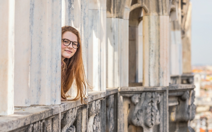 Person peeking through marble columns on Milan Duomo rooftop.