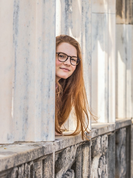 Person peeking through marble columns on Milan Duomo rooftop.