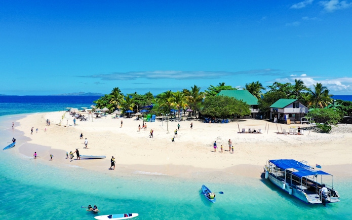 South Sea Cruise boat near tropical island beach with visitors, Fiji.