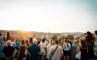 Tourists enjoying a sunset view over Rome from a panoramic vantage point.