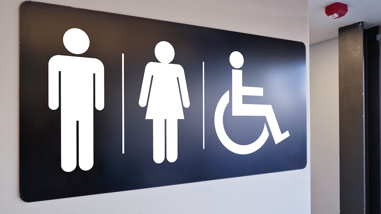 Restroom sign with directional arrow in a busy airport terminal, guiding travelers in New York City.