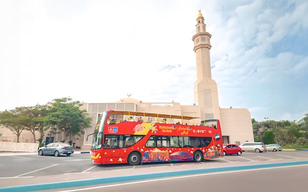 Red double-decker bus on Abu Dhabi hop-on hop-off tour near a mosque.