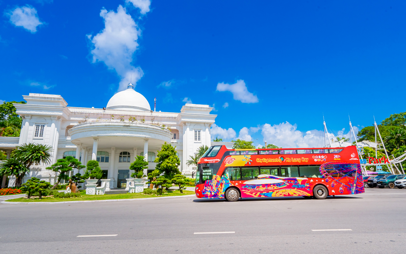 Red sightseeing bus in front of a white domed building in Ha Long Bay.
