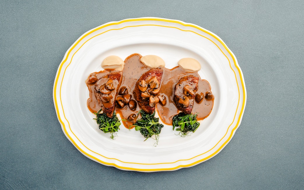 Fricandó dish with mushrooms and greens on a white plate, Berlin.