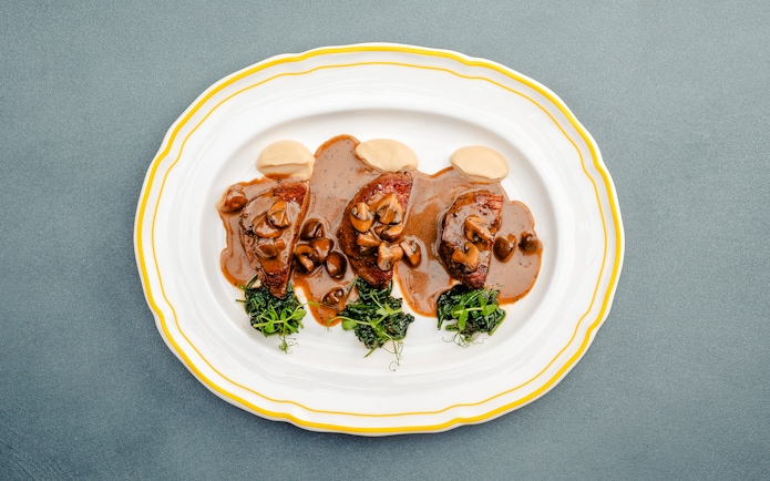 Fricandó dish with mushrooms and greens on a white plate, Berlin.