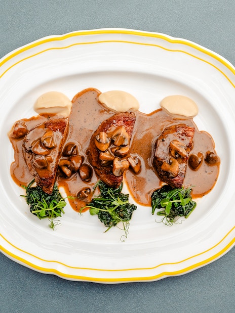 Fricandó dish with mushrooms and greens on a white plate, Berlin.