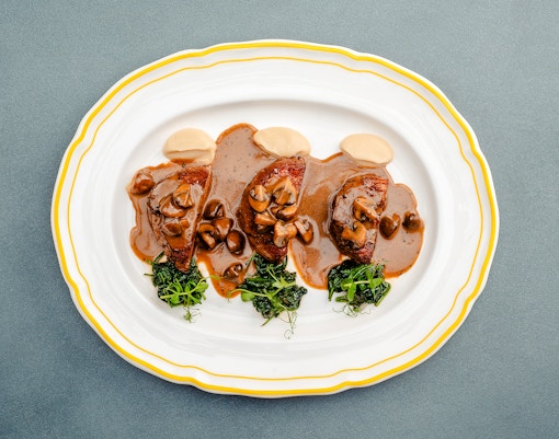 Fricandó dish with mushrooms and greens on a white plate, Berlin.