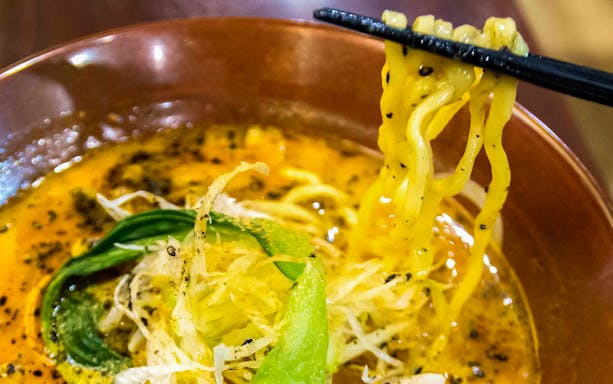 Chopsticks holding ramen noodles over a bowl during Tokyo Ramen Tasting Tour.