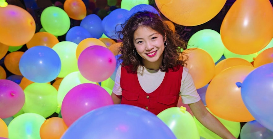 Lady surrounded by colorful balloons at Dopamine Land multisensory experience.