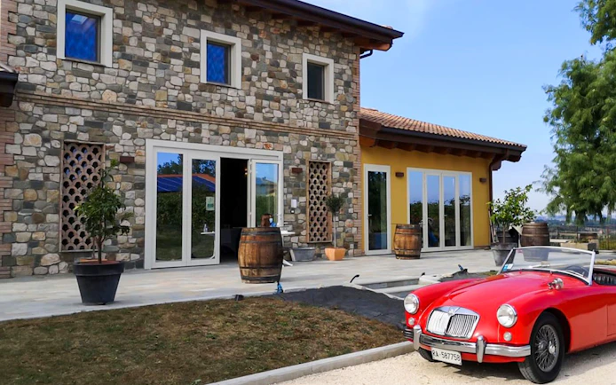 Stone building with barrels outside, red convertible parked, setting for vinegar cellar tour with tastings.
