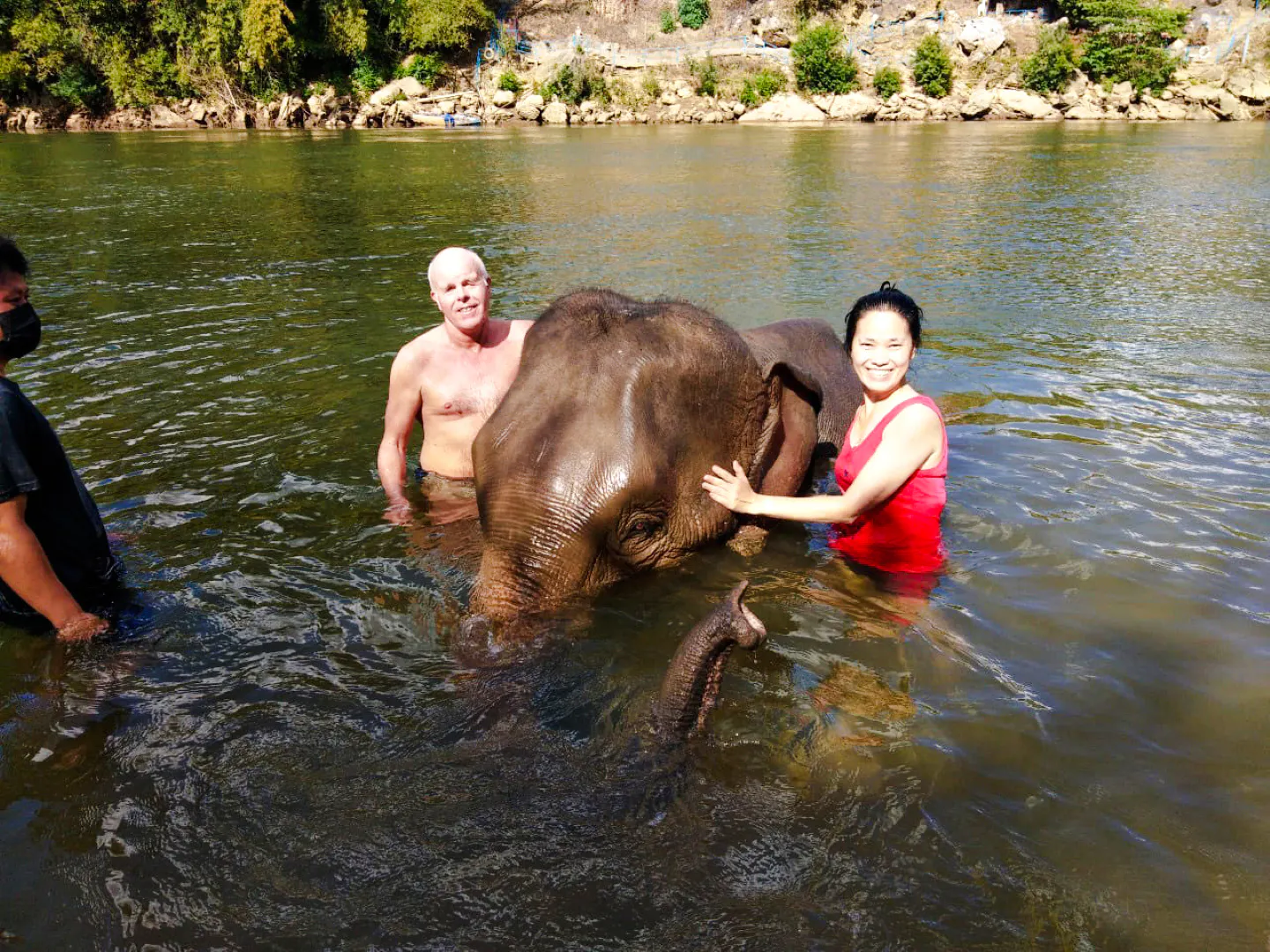 Visitors interacting with an elephant in a river at an ethical sanctuary near Bangkok.