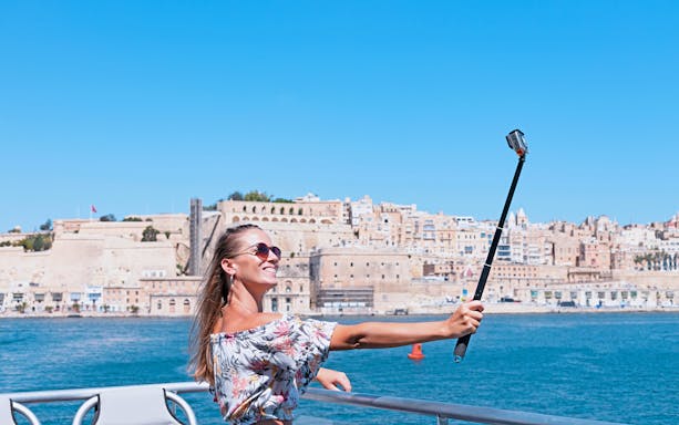 Person taking selfie on a harbour cruise with historic cityscape in the background.