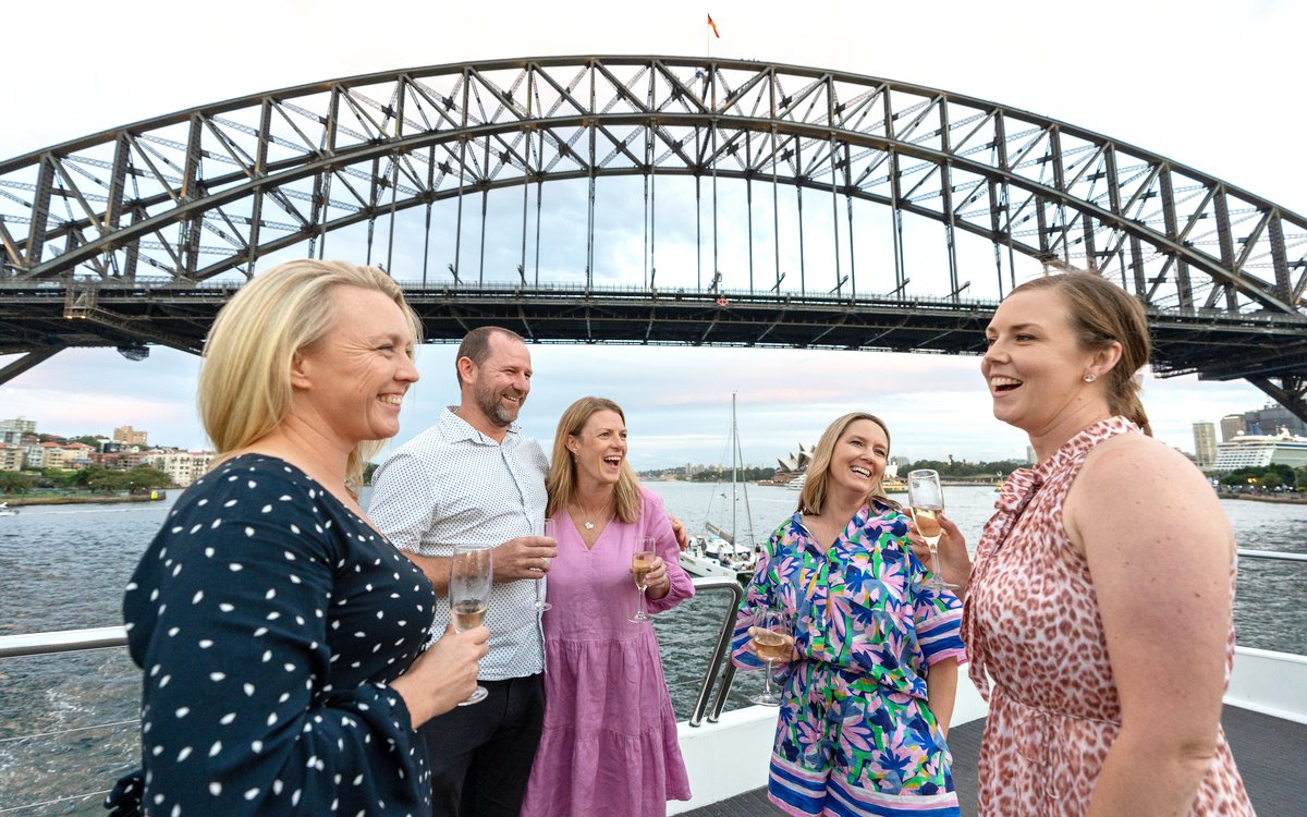 Group enjoying wine on a catamaran with Sydney Harbour Bridge in the background.