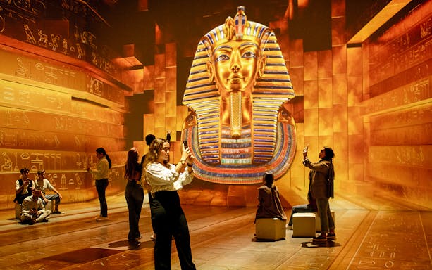 Visitors explore Tutankhamun's golden mask projection at the immersive exhibition.
