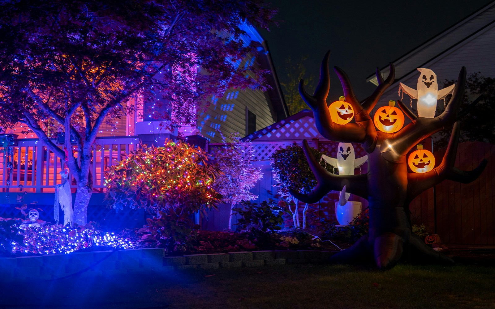Halloween house with glowing inflatable pumpkins, ghosts, purple lights, and orange garlands.