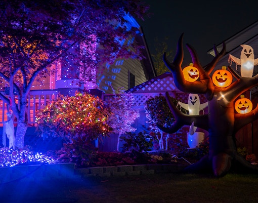 Halloween house with glowing inflatable pumpkins, ghosts, purple lights, and orange garlands.